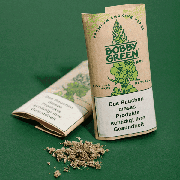 Zwei braune Papierverpackungen mit grünem Bobby Green #01 Logo, Kräutermischung vor den Packungen auf grünem Untergrund.