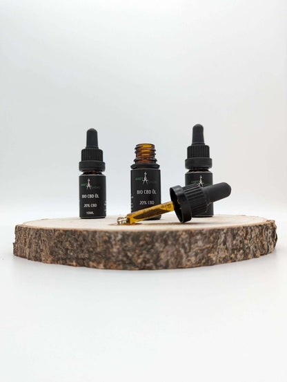 Drei kleine Flaschen Premium Bio CBD Öl mit schwarzem Etikett und Pipetten, eine Flasche offen, auf Holzscheibe platziert.